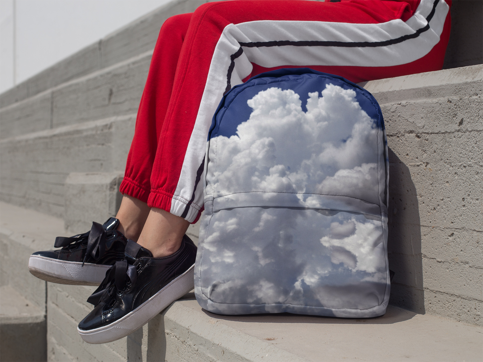 Person Sitting on Cement Stairs With a Backpack Featuring Mostly Clouds - Front View